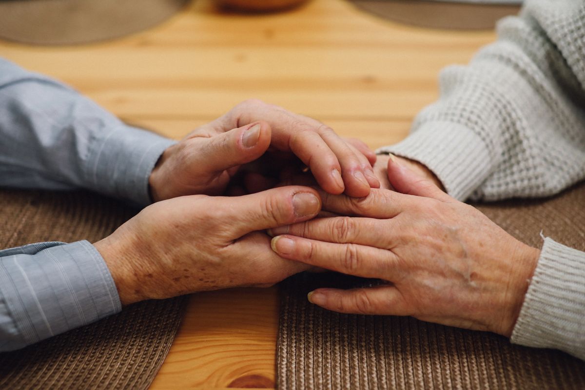 Two pairs of older hands rest together on a wooden table